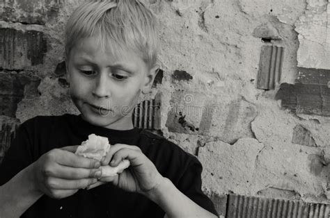 Een Hongerige Vuile Jongen Eet Greedily Een Korst Van Brood Tegen De Muur Toning Stock
