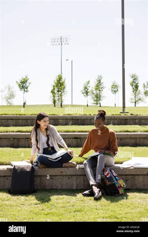 Happy Young Female College Students Studying In Grass On Sunny Campus