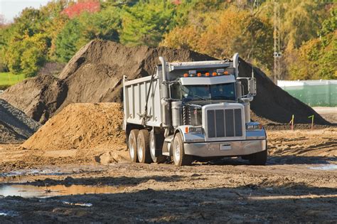 A Dump Truck About To Unload A Pile Of Dirt At An Excavation Site