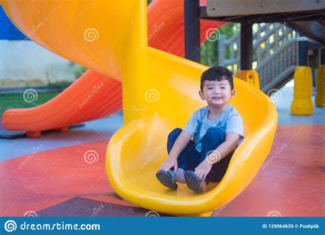 Asian Kid Playing Slide At The Playground Under The Sunlight In Stock
