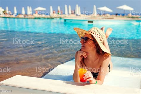 Woman Relaxing In Hotel Swimming Pool Lying On Chaiselongue With