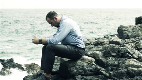 Sad Man Sitting Alone On Rocks Next To The Sea Stock