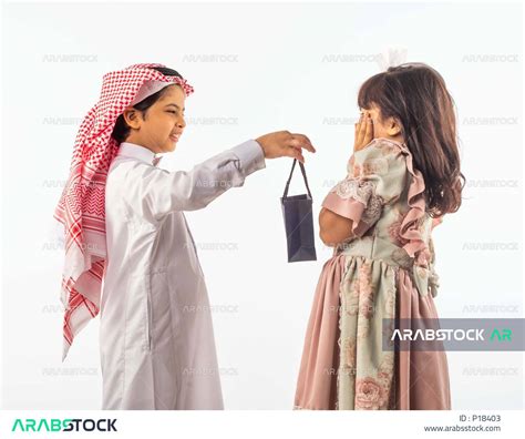 خلفية بيضاء لصبي وفتاه صغيران سعوديان مبتسمان ، الفتاه الصغيرة تضع يدها على خدها تشعر بالخجل