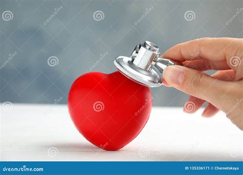 Woman Holding Stethoscope Near Red Heart On Wooden Table Closeup