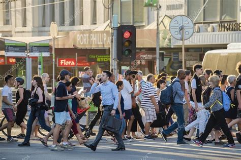 People Walking Across A Busy Crosswalk In Melbourne At Sunset Stock