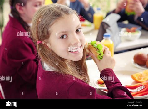 Beautiful Girl Eating Delicious Food While Sitting At Dining Table In School Cafeteria Stock