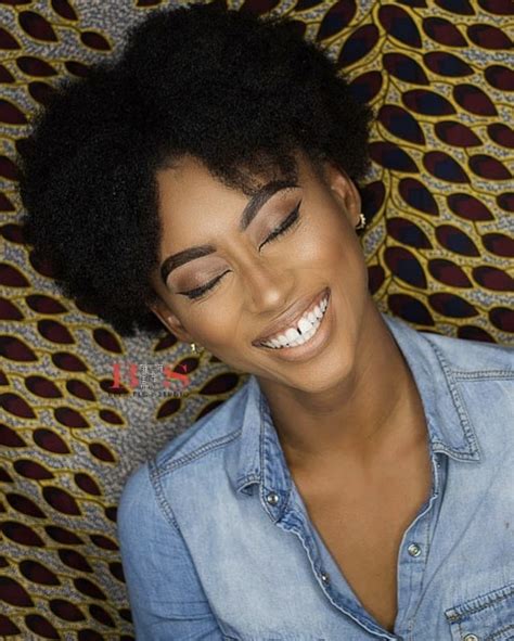 a woman with an afro is smiling and looking at the camera while wearing a denim shirt