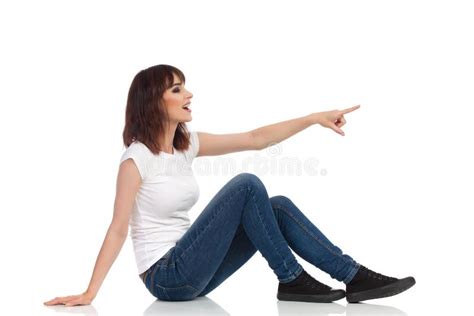 Happy Young Woman Is Sitting On Floor Pointing Looking Away And Talking Side View Stock