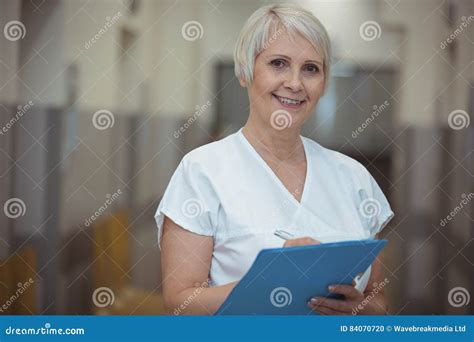 Portrait Of Female Nurse Writing On Clipboard In Corridor Stock Photo