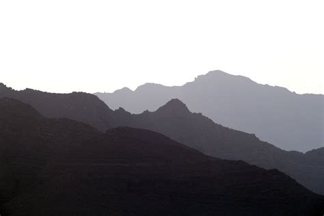 Dark Silhouettes Of Rocky Mountain Ridges Under A Pale White Sky