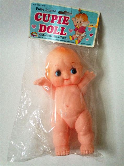 A Pink Doll With Blue Eyes Sitting On Top Of A Plastic Bag In The Shape