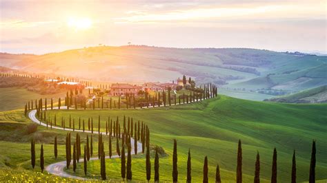 A car driving through picturesque Italian countryside with rolling hills and vineyards.