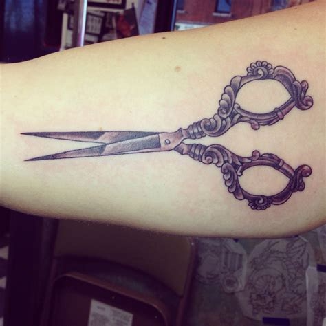 Scissors and a tiny Om symbol tattooed on the forearm