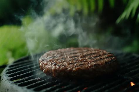 A person's hands selecting ground beef from a butcher shop display case.