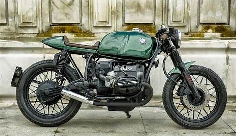 Green cafe racer motorcycle parked on the side of a dirt road. - Stock