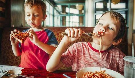 Kinder essen Pizza, Pasta und Salat im traditionellen Restaurant