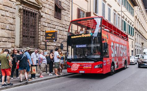 A smiling couple taking pictures while sitting on the top deck of a sightseeing bus