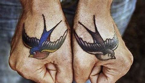 A hand holding a small sparrow tattoo on the left upper