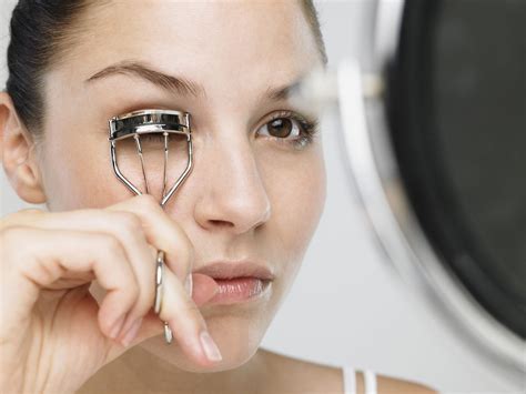 Curling your eyelashes with an eyelash curler while applying mascara at