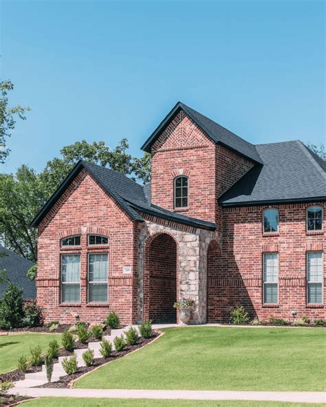 Traditional style red brick home with black roofing and sandy stone