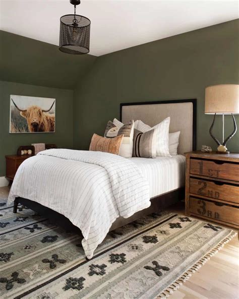 Image of a cozy rustic bedroom with sage green walls, exposed wooden beams, and a stone fireplace.